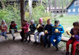 Dzieci siedzą trzymając wosk pszczeli na drewnianych ławkach.